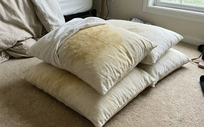 A pile of old, flattened pillows on a bedroom floor